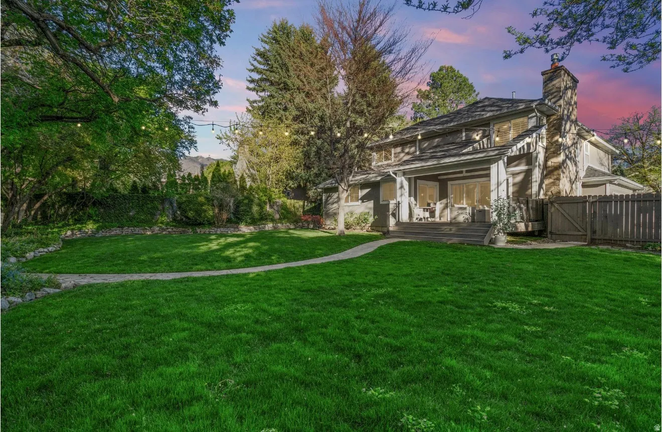 Expansive rear yard featuring a stone pathway, mature trees, and a wooden privacy fence