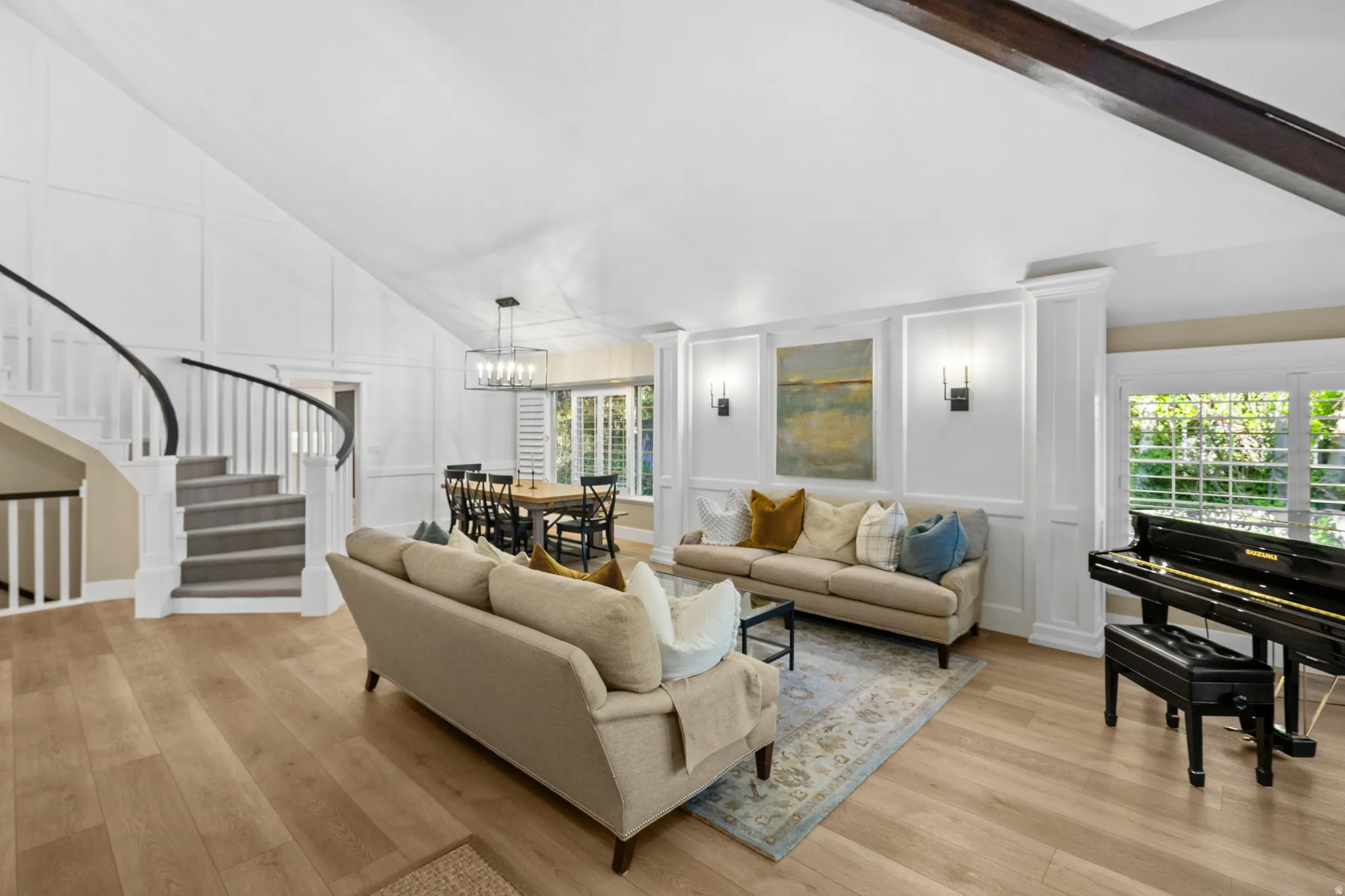 Open-concept living area featuring light wood-finish flooring, a grand curved staircase with carpeted treads, and extensive wainscoting