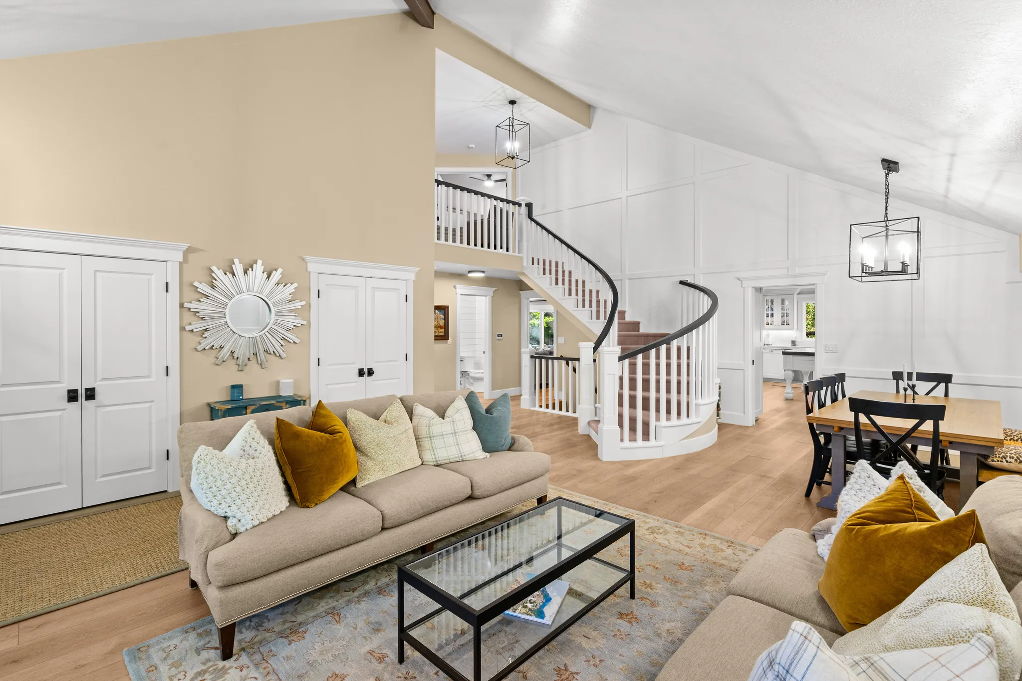 Open-concept living space featuring vaulted ceilings, wood-finish flooring, a spiral staircase with a black handrail and white balusters, and a dining area with a wood-top table