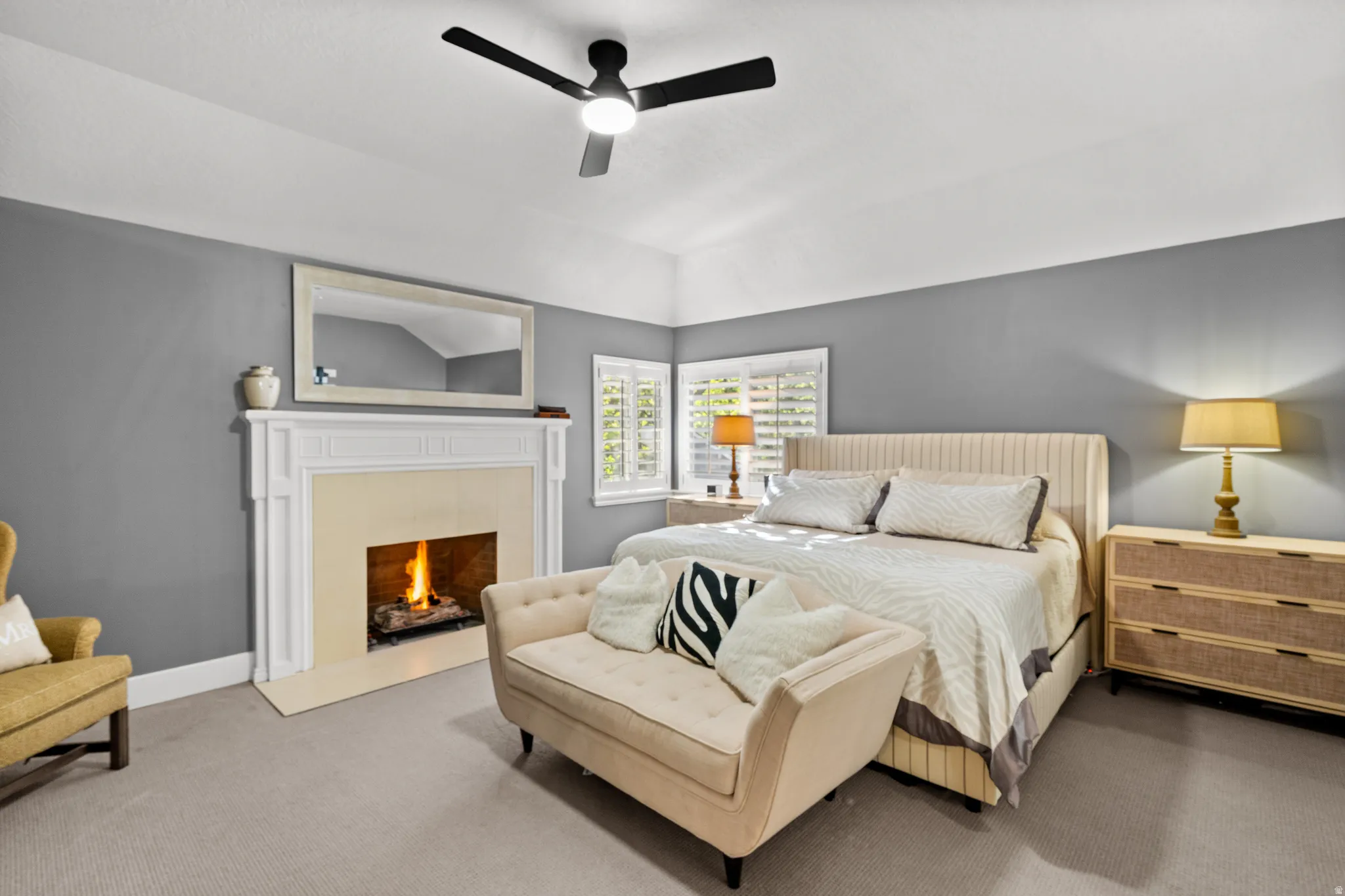 Bedroom featuring a decorative fireplace with a white mantel, ceiling fan, and plantation shutters
