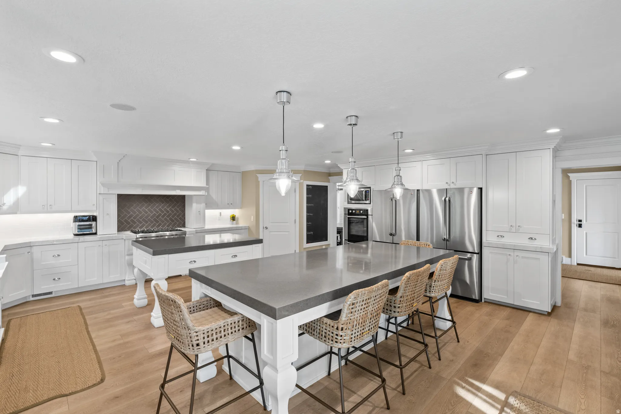 Kitchen featuring two islands with solid surface countertops, extensive white cabinetry, stainless steel appliances, herringbone tile backsplash, and light wood-finish flooring