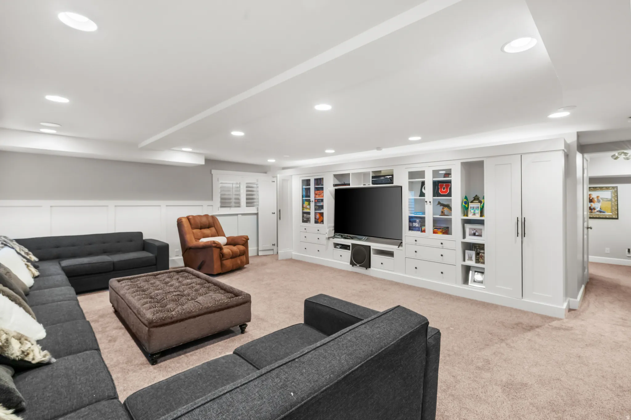Recessed lighting illuminates a spacious room featuring a comprehensive built-in entertainment center with integrated cabinetry and shelving