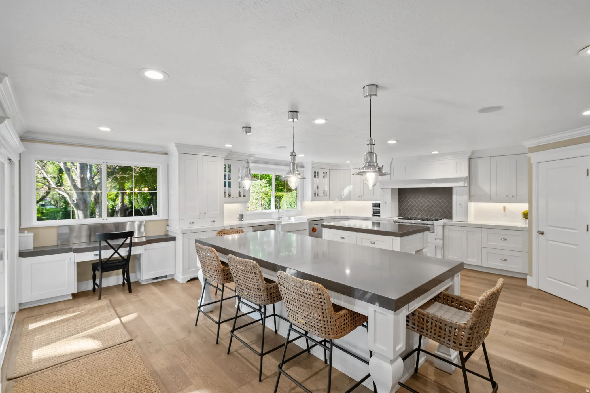 Spacious kitchen featuring two large islands with countertop seating, white shaker cabinetry, recessed lighting, and wood-finish flooring