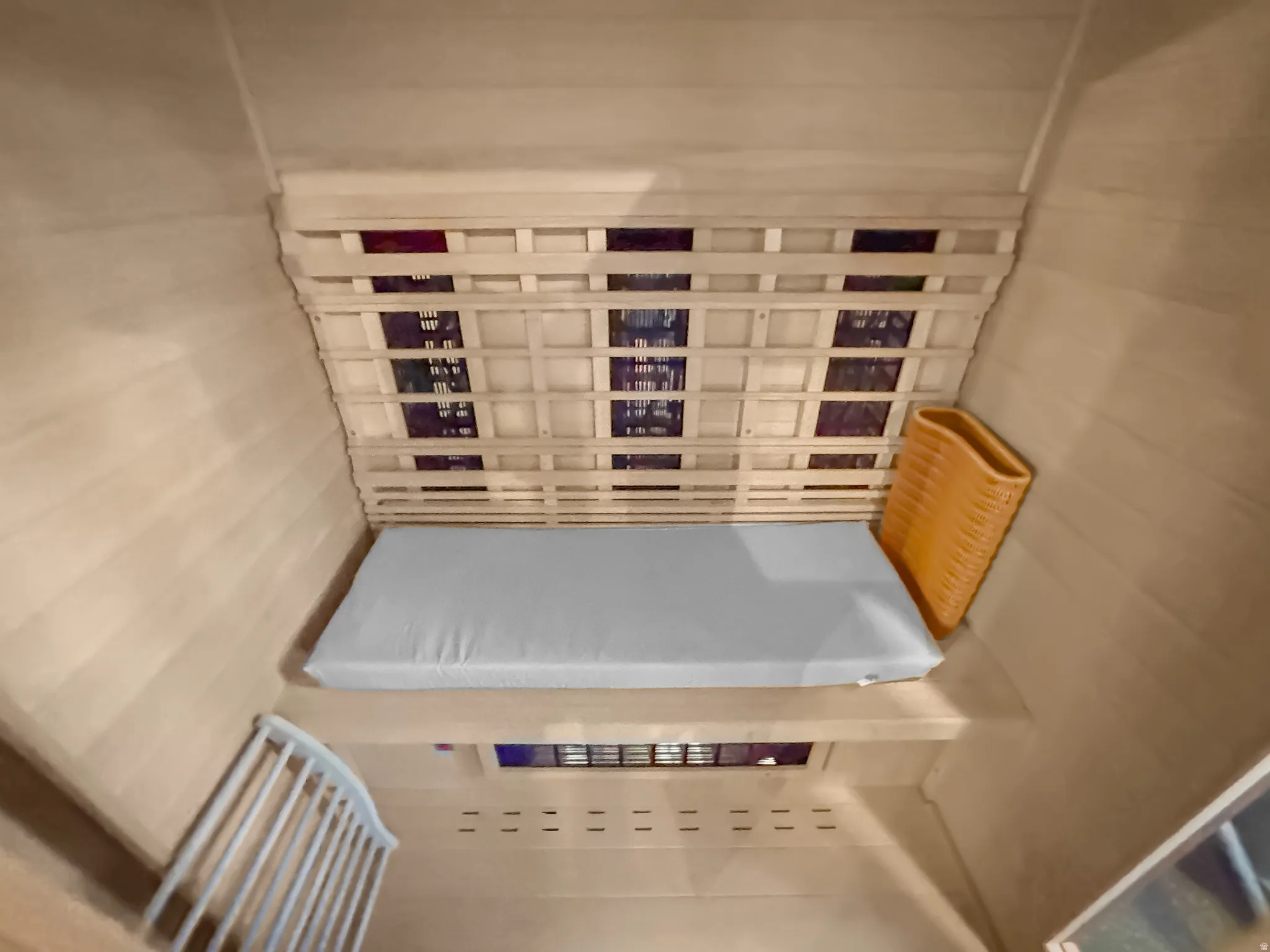 Interior sauna space featuring light wood paneling, slatted wood backrest, and a built-in bench with a light-colored cushion