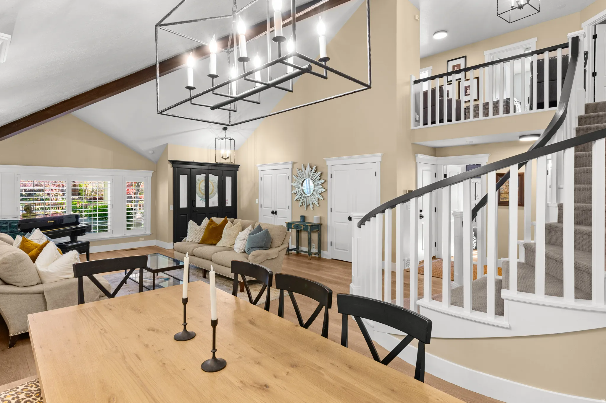 Spacious living area featuring a vaulted ceiling with exposed wood beams, a large decorative chandelier, and wood-finish flooring