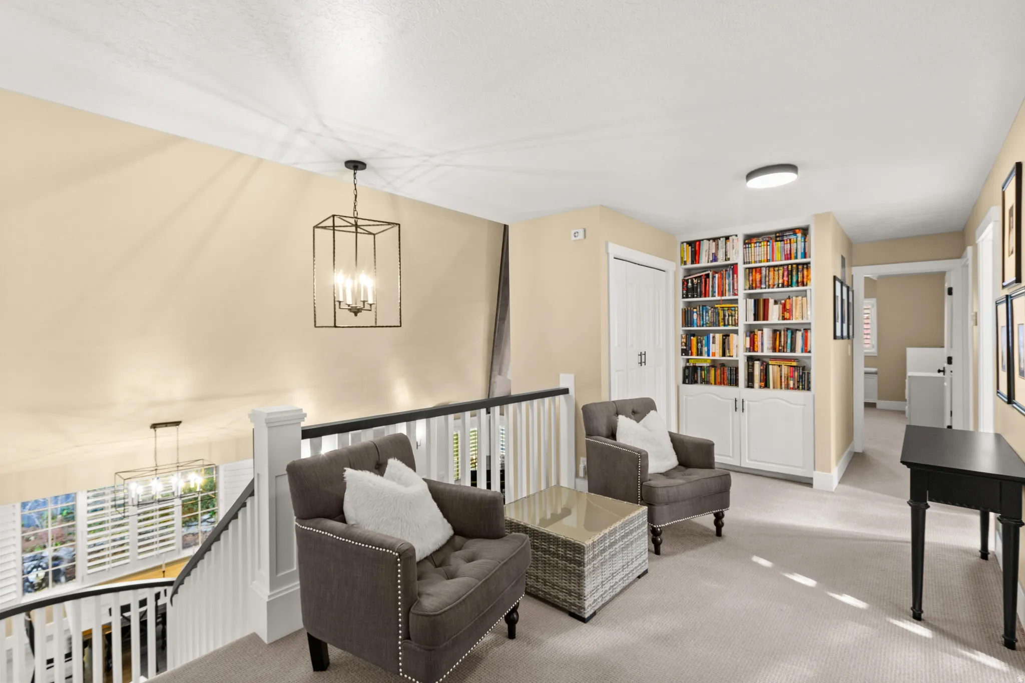 Upper-level landing featuring a built-in bookcase with lower cabinetry, a staircase with a white and dark wood railing, and a pendant light fixture
