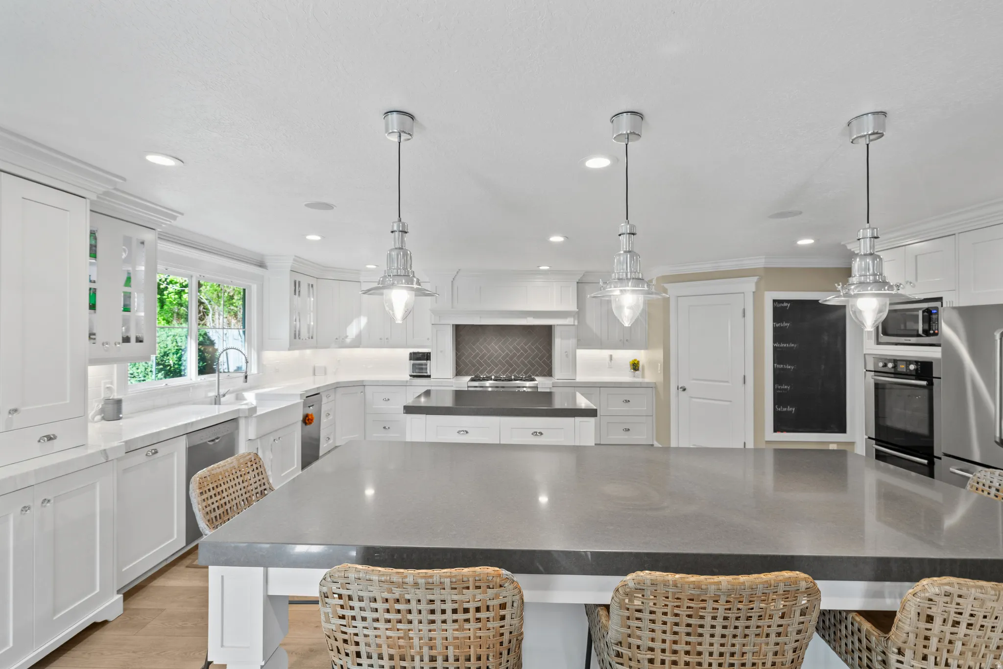 Spacious kitchen featuring a large central island with a grey countertop, white cabinetry, integrated stainless steel appliances, pendant lighting, and a subway tile backsplash