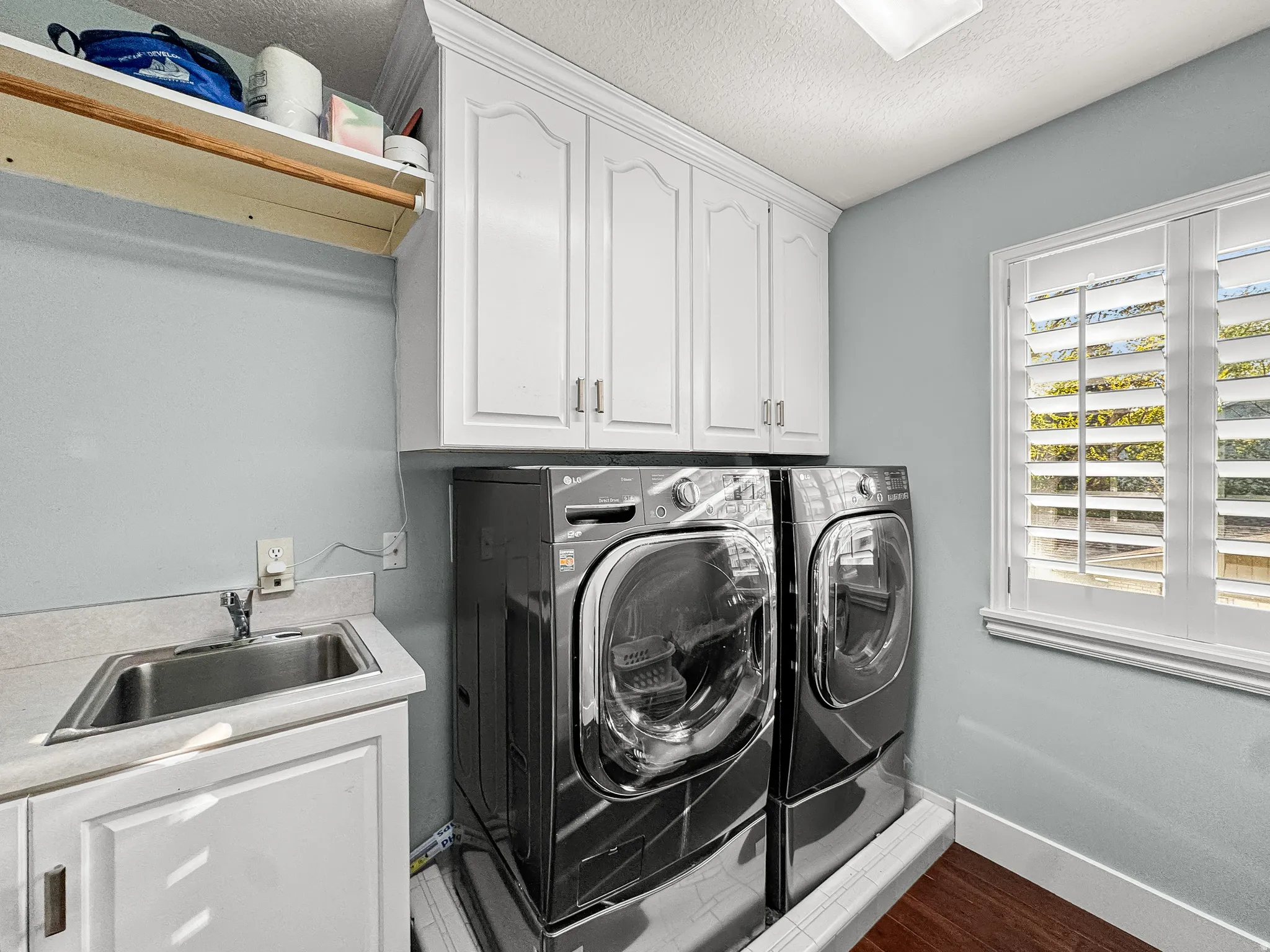 Laundry area featuring white cabinetry, a utility sink with a laminate countertop, and wood-finish flooring