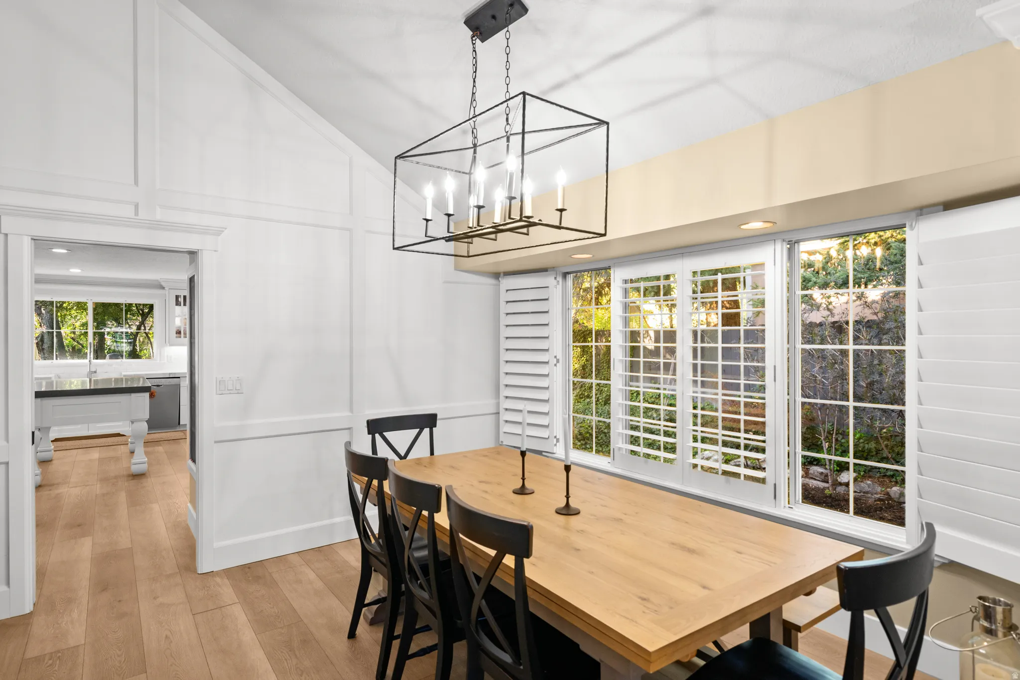 Dining area featuring a vaulted ceiling with board and batten wall details, wood-finish flooring, and a black open-frame chandelier