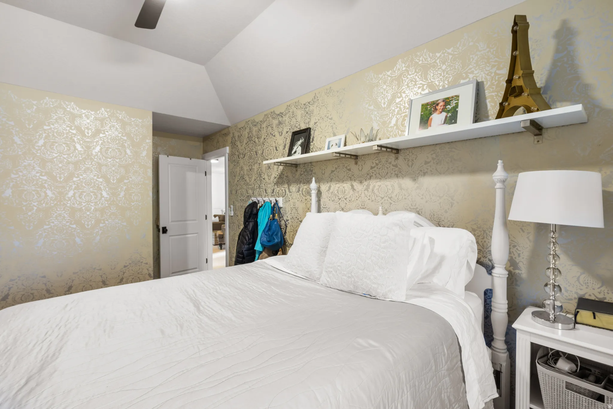 Vaulted ceiling bedroom featuring decorative patterned wallpaper, a paneled interior door, and built-in wall shelving
