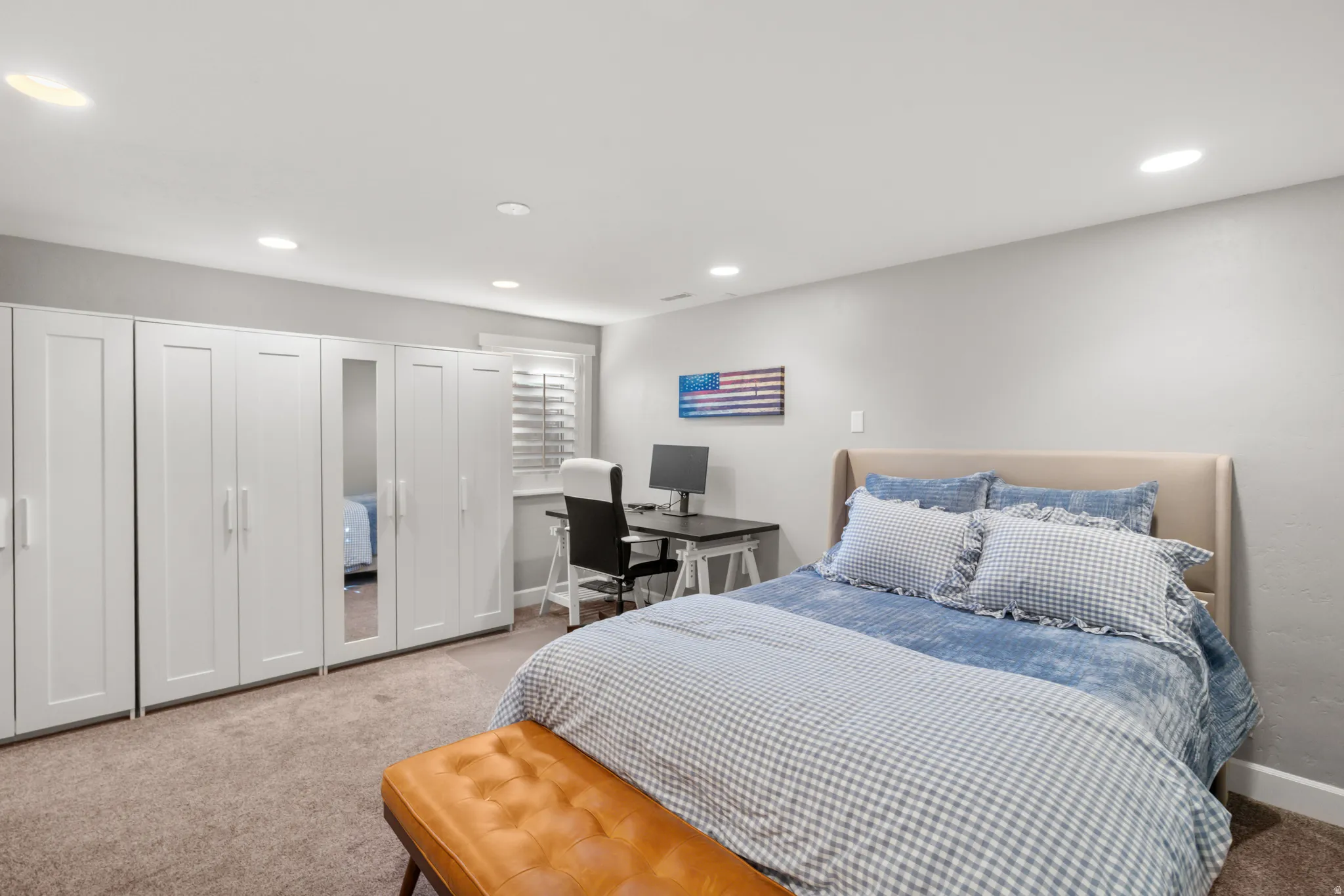 Recessed lighting illuminates an interior space featuring a bed with a fabric headboard