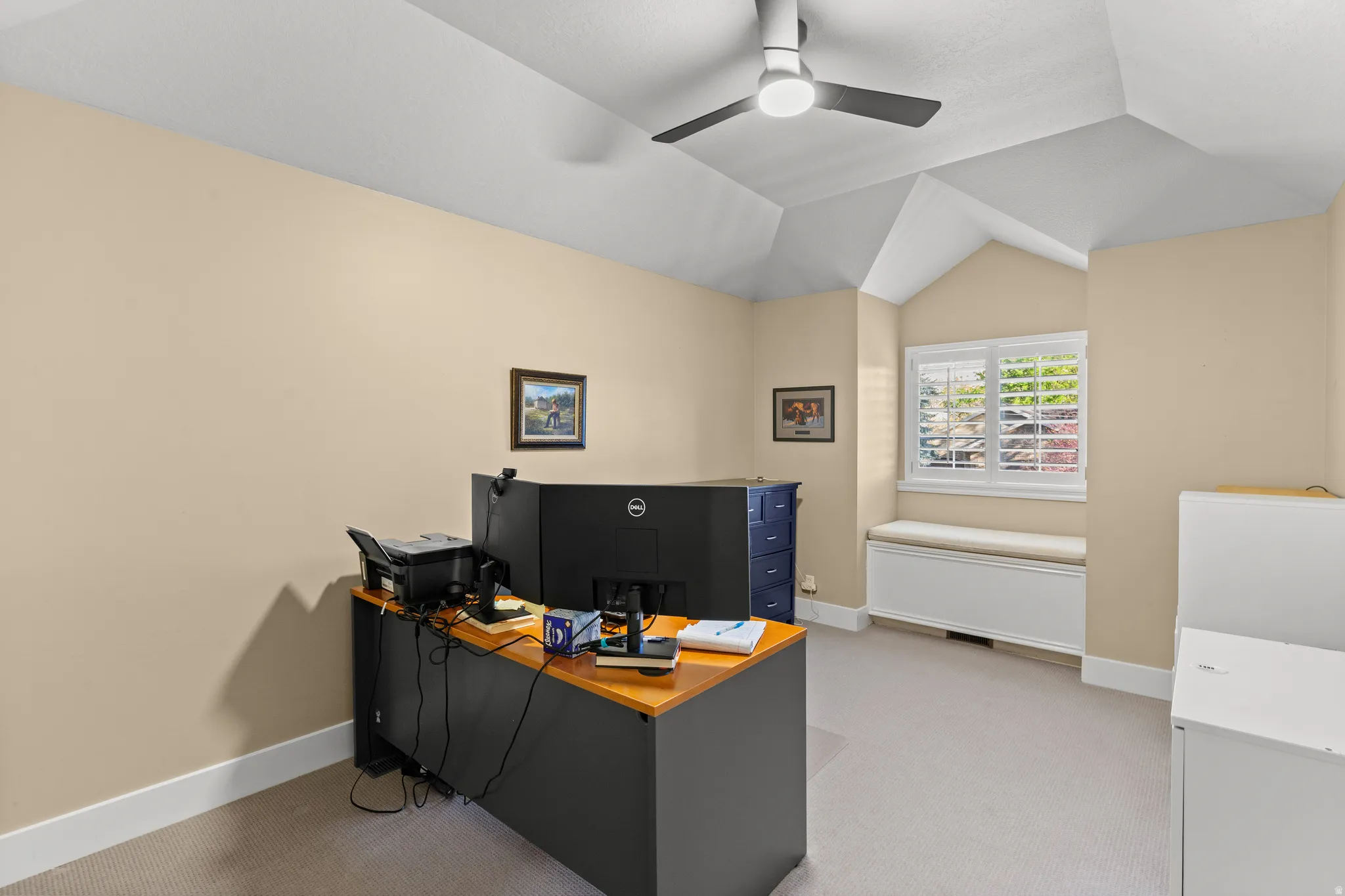 Vaulted ceiling room featuring a window with plantation shutters, a built-in window seat, and a contemporary ceiling fan