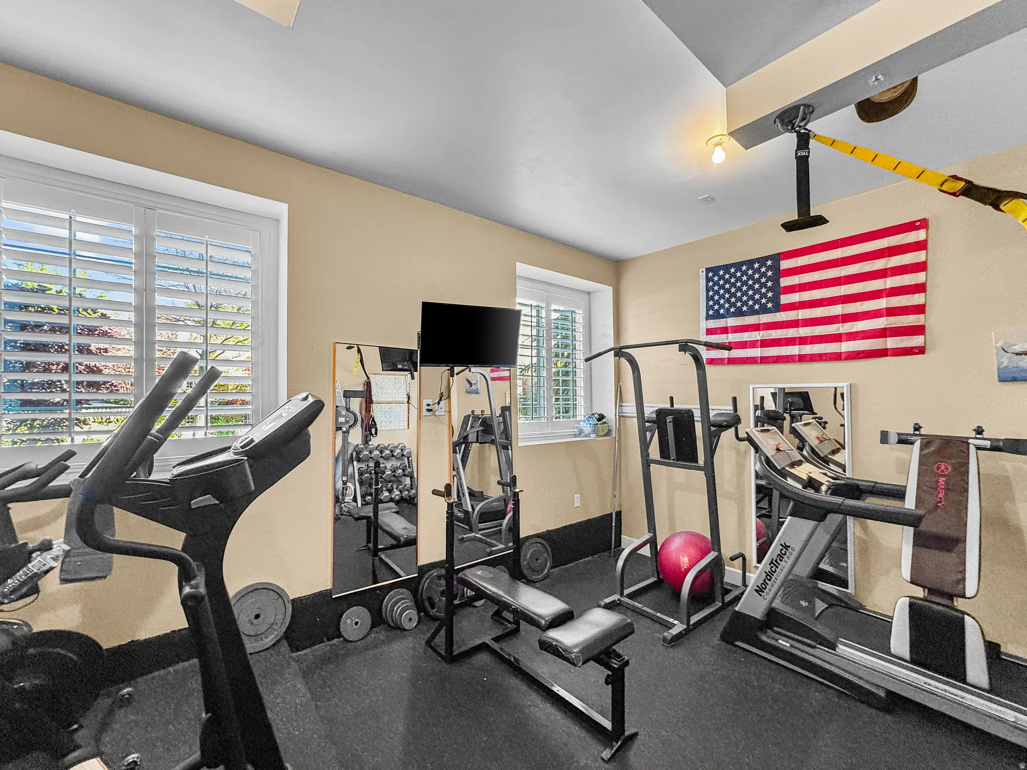 Dedicated room featuring black rubberized flooring, light tan wall color, and white plantation shutters