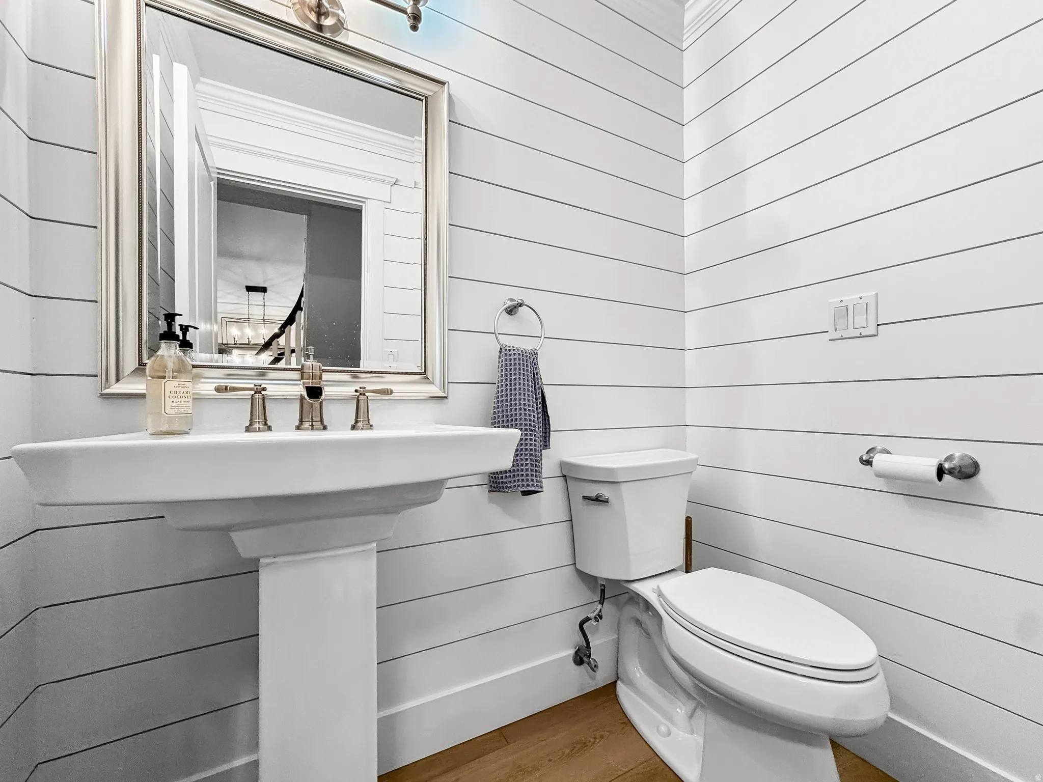 Pedestal sink with a brushed nickel faucet set, framed mirror, and shiplap wall paneling