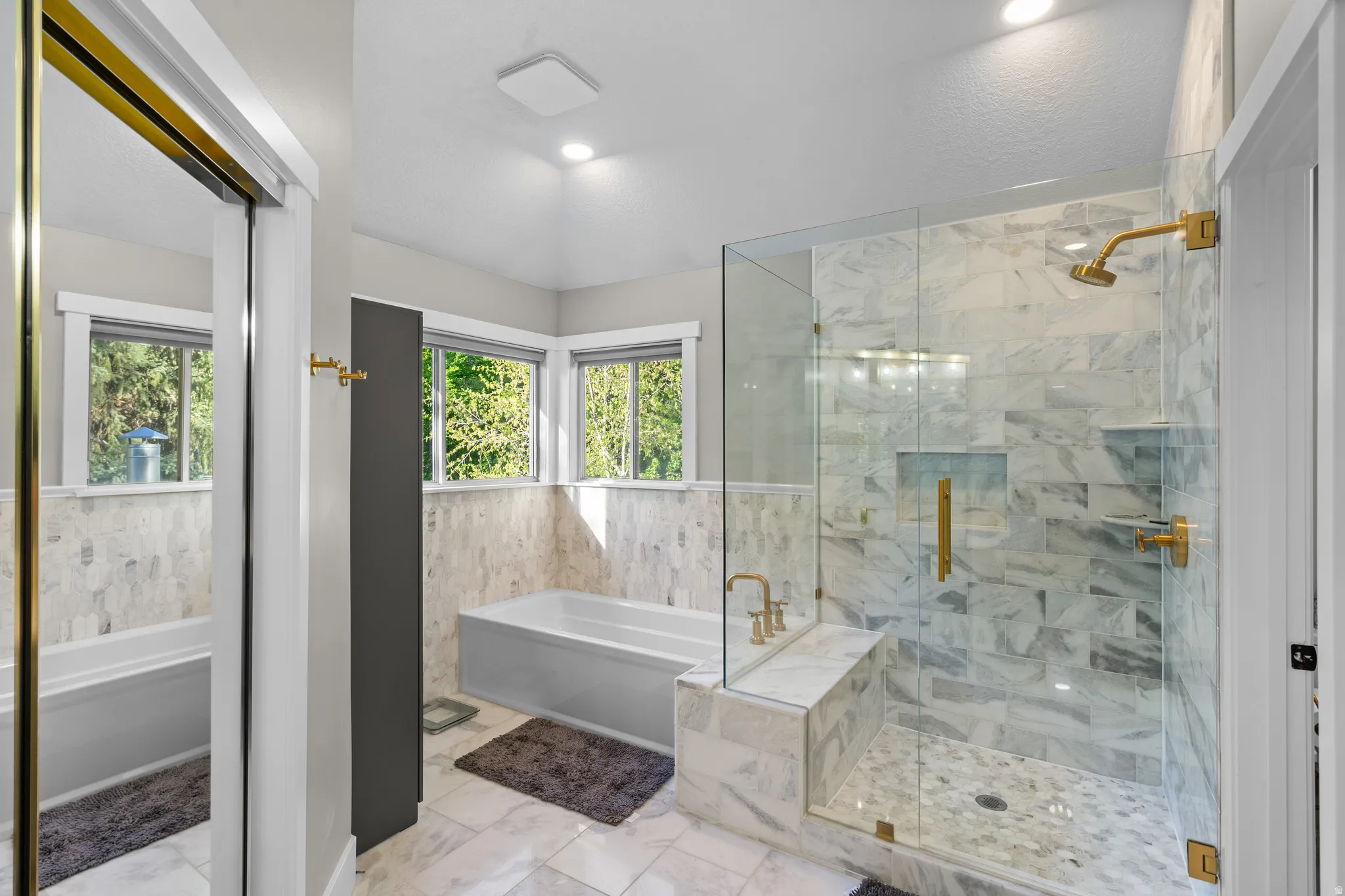Master Bathroom featuring a glass-enclosed shower with a built-in bench, a separate soaking tub, multiple windows, and gold-finish fixtures