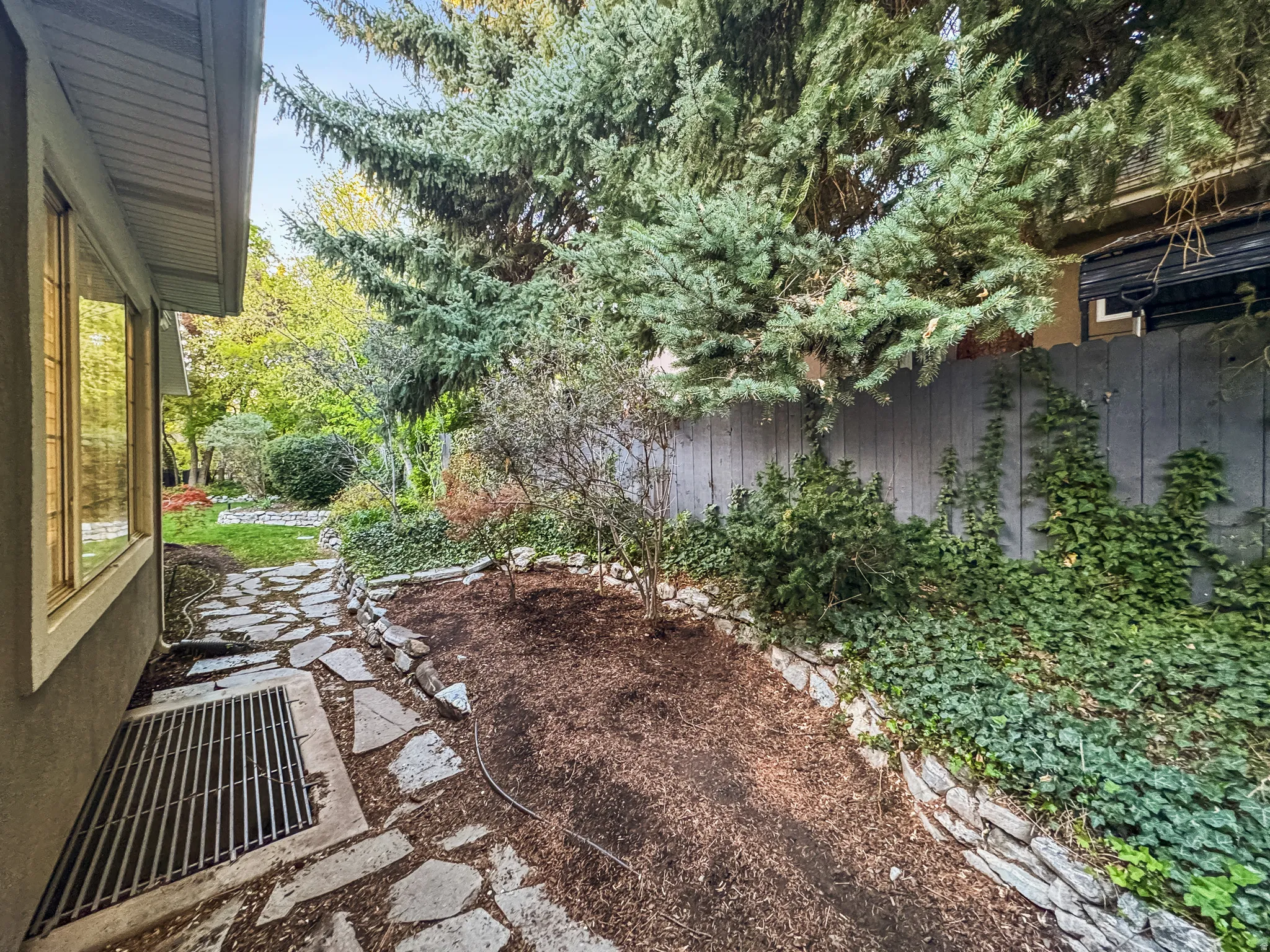 Stone pathway alongside the property, bordered by a planted garden bed with bark mulch and varied greenery