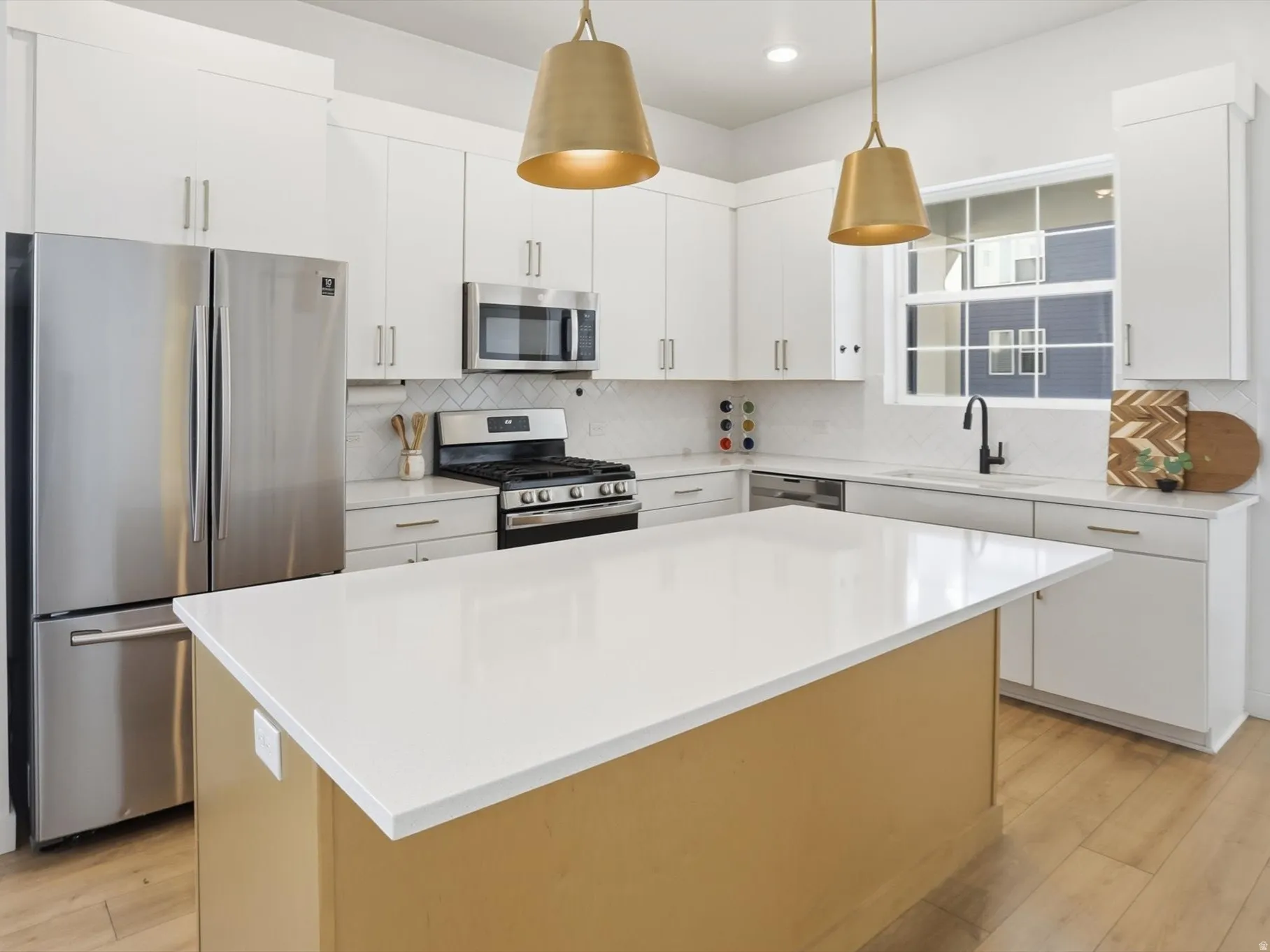Modern kitchen featuring white cabinetry, stainless steel appliances, gas range, two-tone white and oak cabinetry, brass hardware, refined designer finishes, an oversized sink-free island, and walk-in pantry.