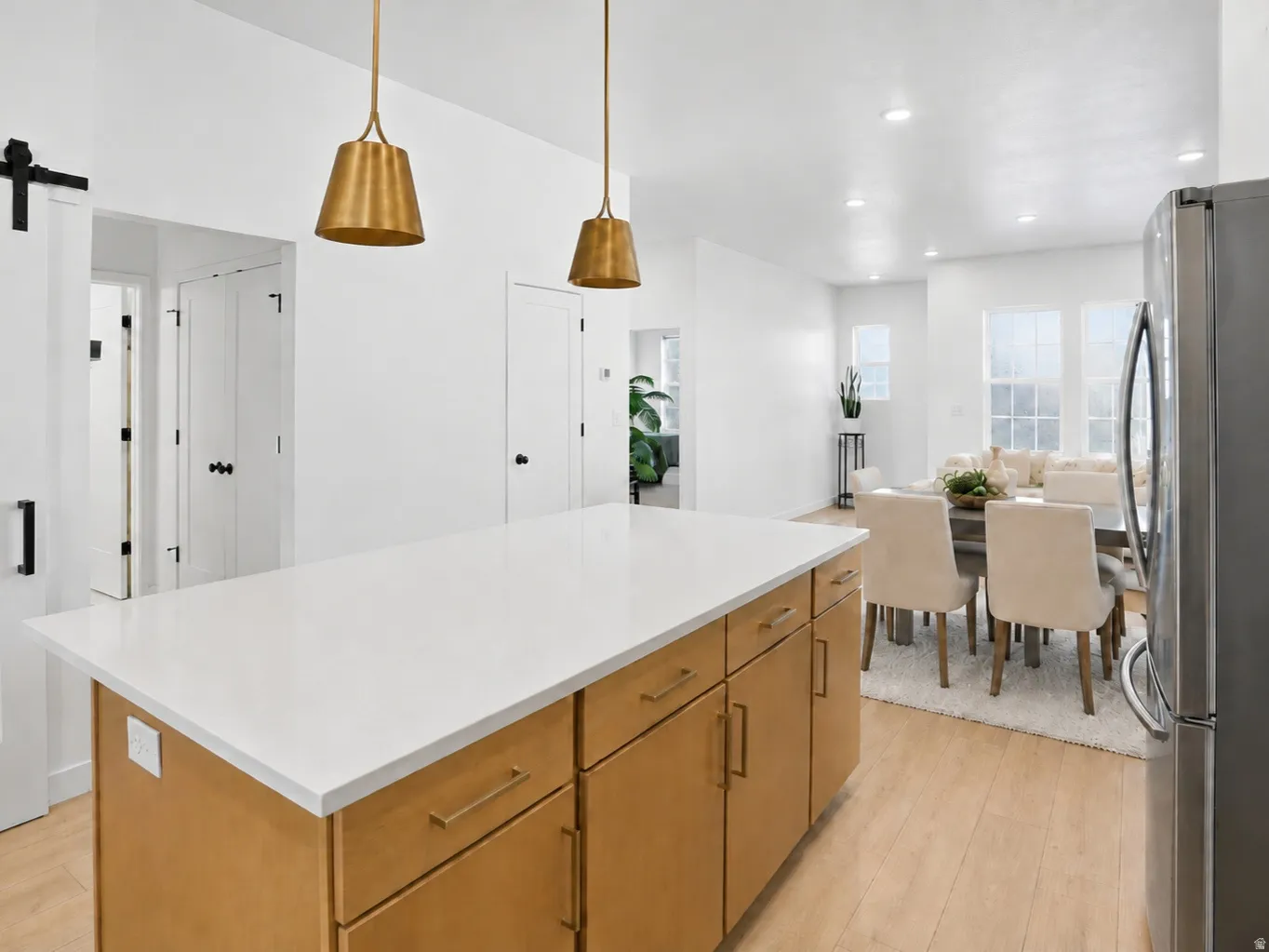 Modern kitchen featuring white cabinetry, stainless steel appliances, gas range, two-tone white and oak cabinetry, brass hardware, refined designer finishes,, an oversized sink-free island, and walk-in pantry.