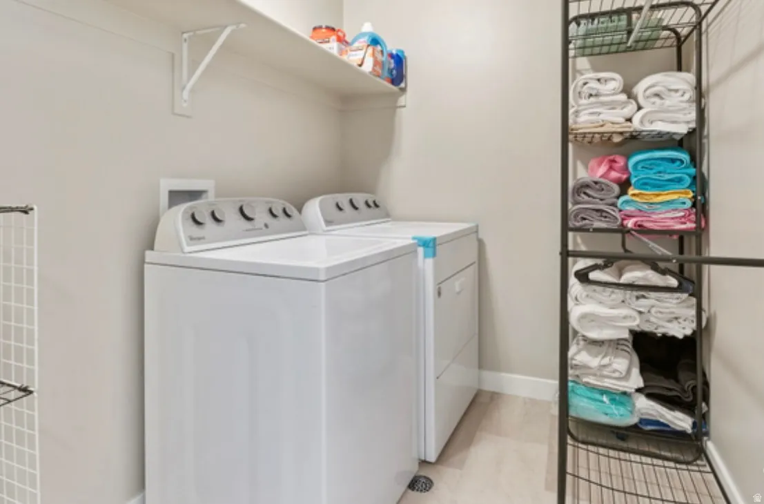 Dedicated laundry space featuring a white top-load washer and dryer set, a wall-mounted storage shelf, and light wood-finish flooring