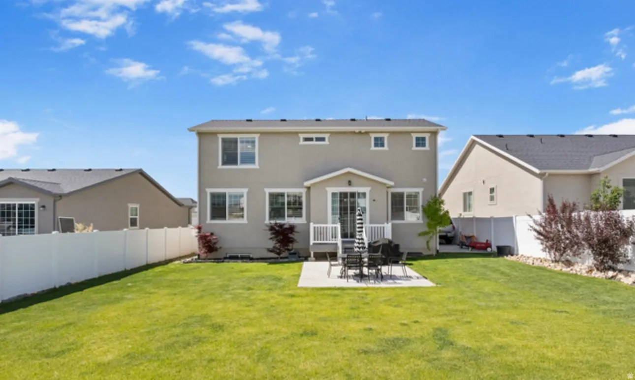 Spacious green lawn featuring a concrete patio, white vinyl fencing, and a rear stucco exterior