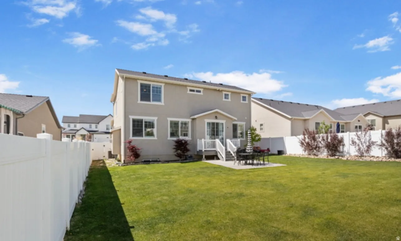 Spacious backyard featuring a manicured lawn, white privacy fencing, and a concrete patio