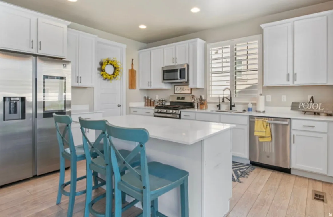 Kitchen featuring white shaker-style cabinetry, stainless steel appliances, a center island with a solid surface countertop, and wood-finish flooring