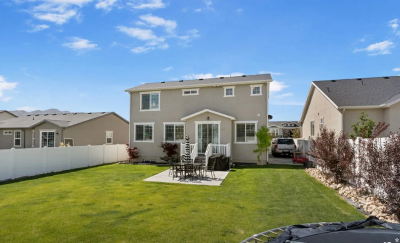 Expansive backyard with a manicured lawn, concrete patio, and white vinyl perimeter fencing