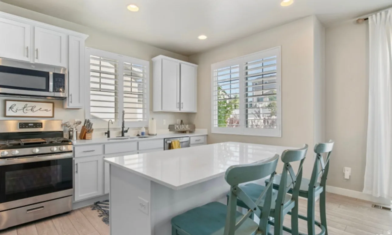 Modern kitchen featuring white shaker cabinetry, stainless steel appliances, a center island with a white countertop, and plantation shutters