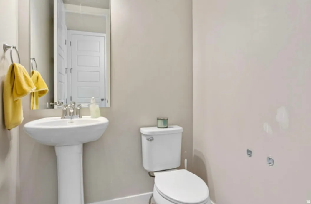 Bathroom featuring a white pedestal sink with a chrome faucet, a rectangular wall-mounted mirror, and a white toilet