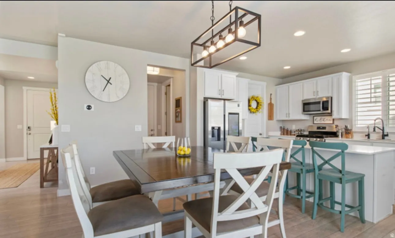 Open-concept kitchen and dining area featuring light wood-finish flooring, white cabinetry, stainless steel appliances, and a central island with a sink