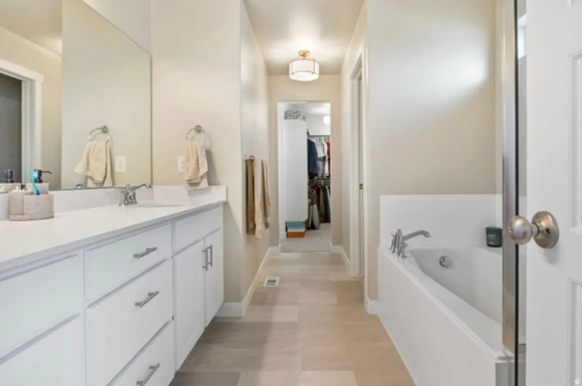 Bathroom featuring a double vanity with white cabinetry and a light-toned countertop, a built-in soaking tub, and tile flooring