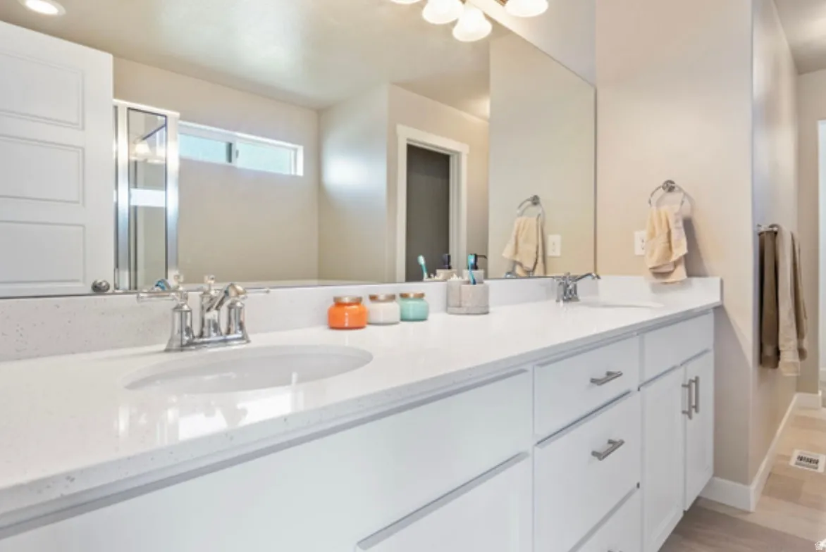 Dual vanity featuring white cabinetry with brushed nickel hardware, integrated sinks, a light-colored countertop, and an expansive wall mirror