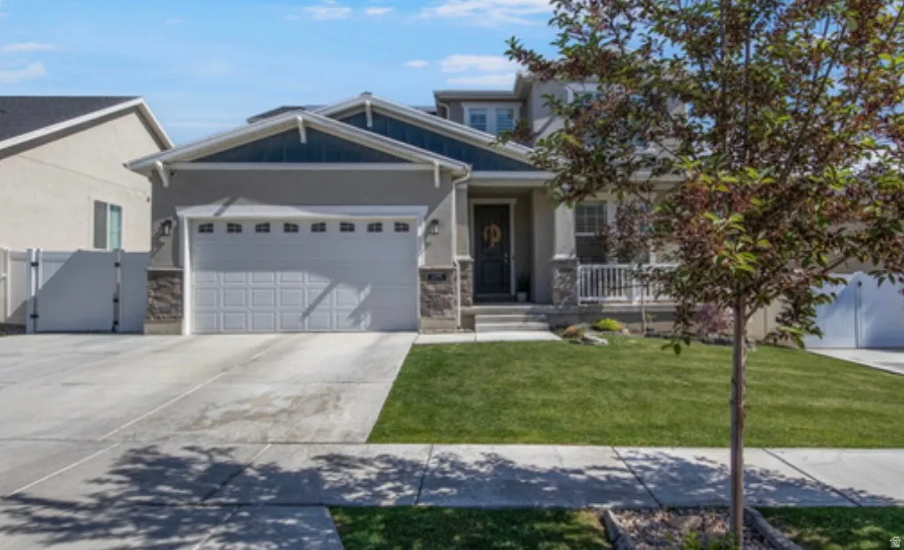 Contemporary stucco exterior with stone accents, a two-car garage, a covered front porch, and a lush green lawn