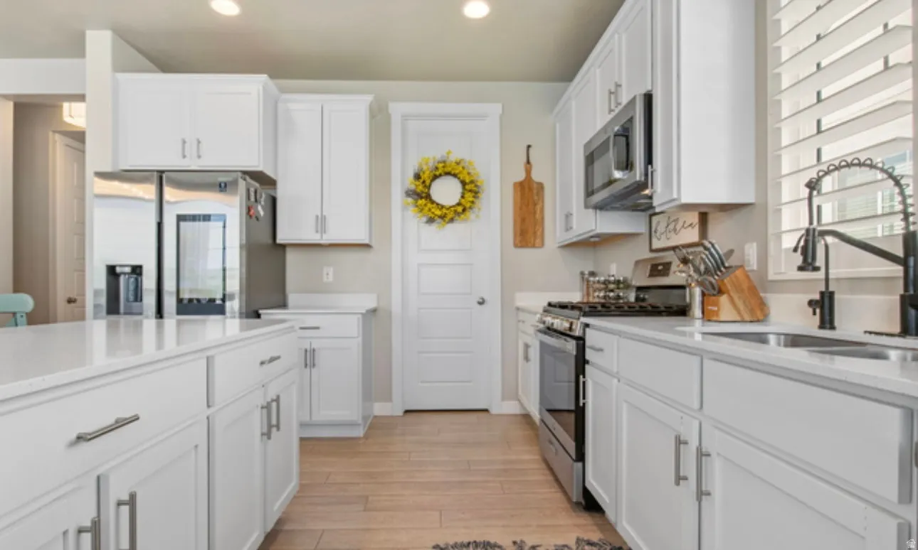 Kitchen featuring white shaker-style cabinetry, light-toned countertops, stainless steel appliances, a center island, and wood-finish flooring