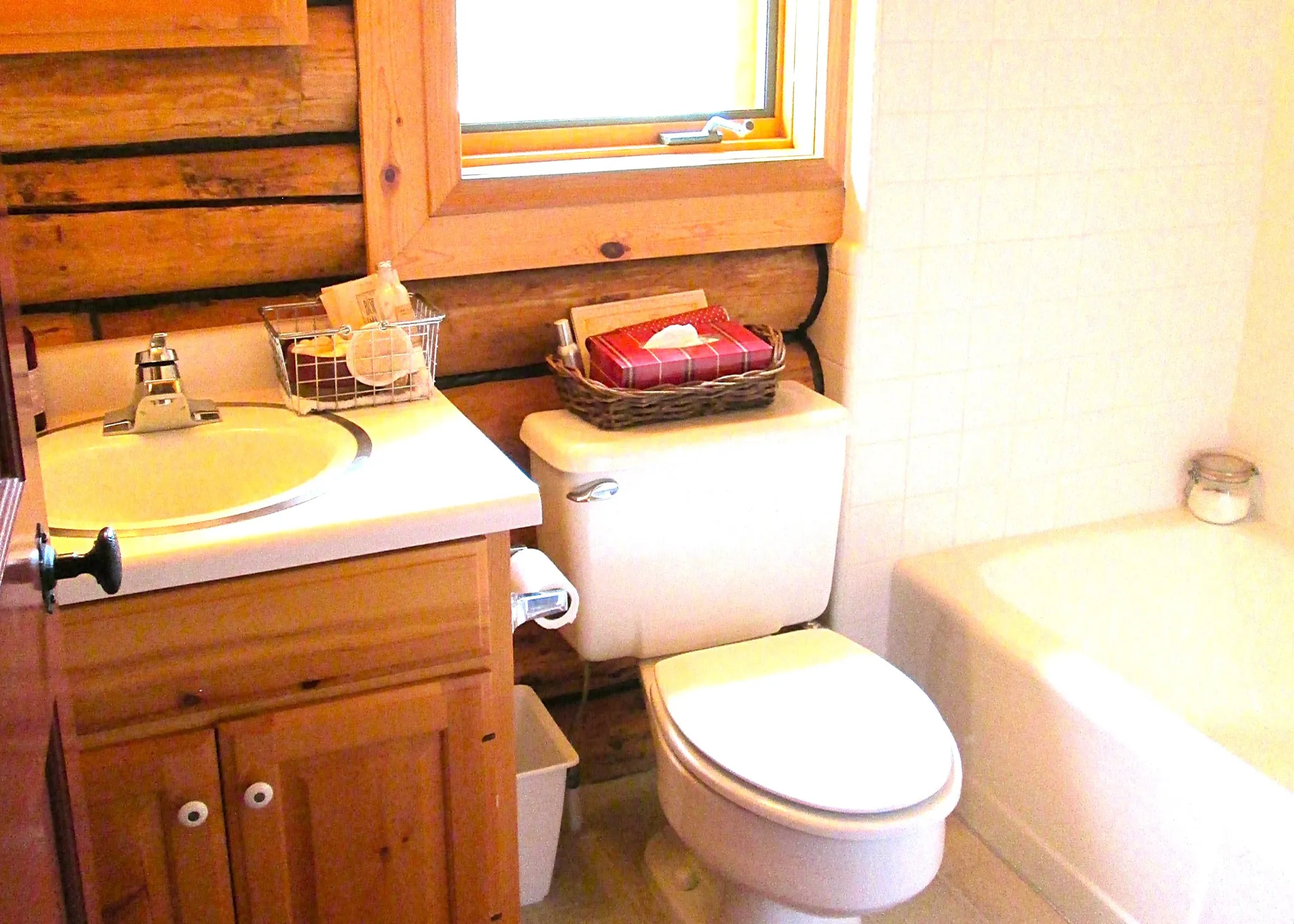 The main floor bath features a pine vanity, pine medicine cabinet, & casement window with red Roman shade.