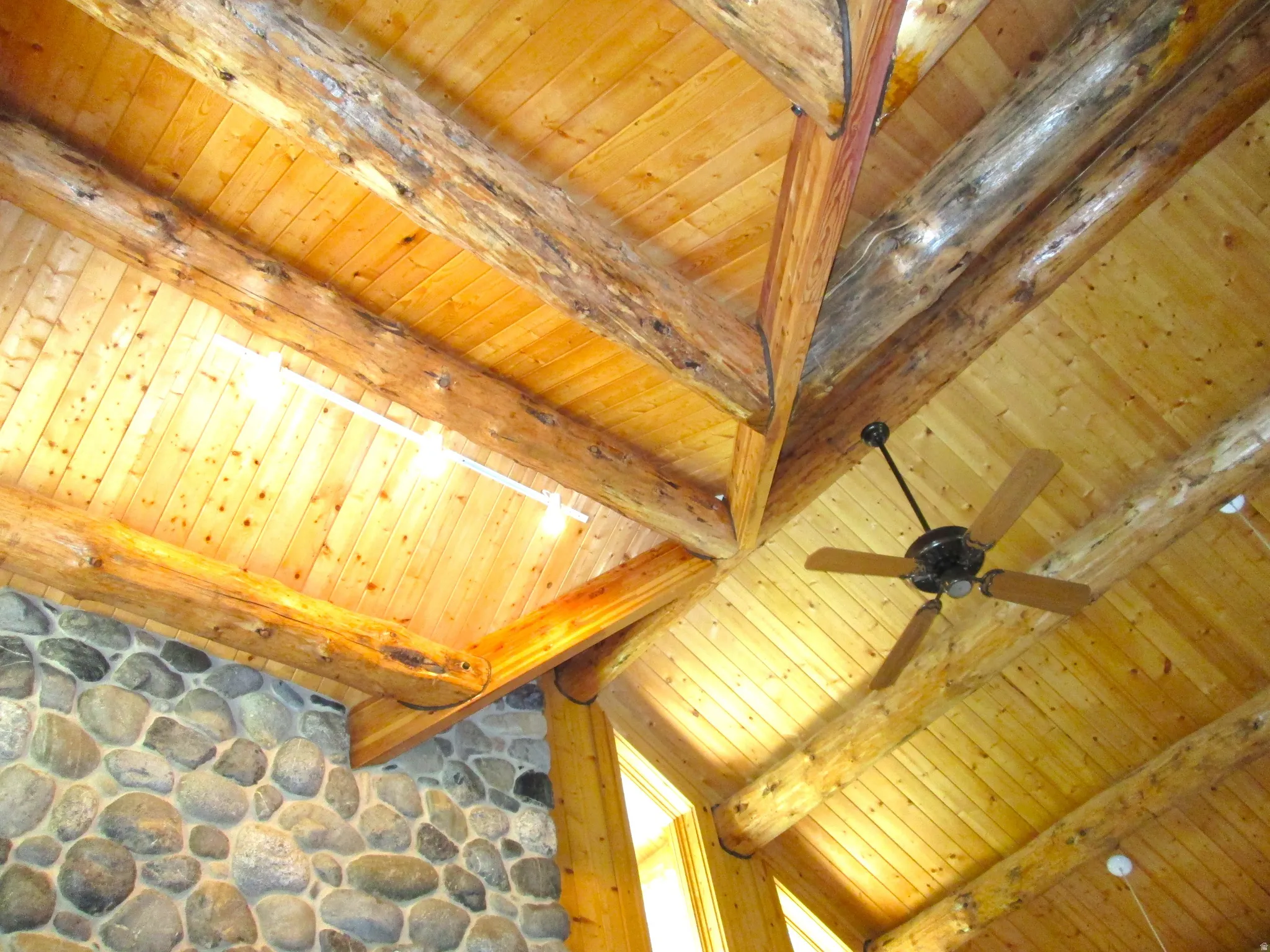 Detailed view of the vaulted great room ceiling with exposed log beams and a remote controlled ceiling fan.