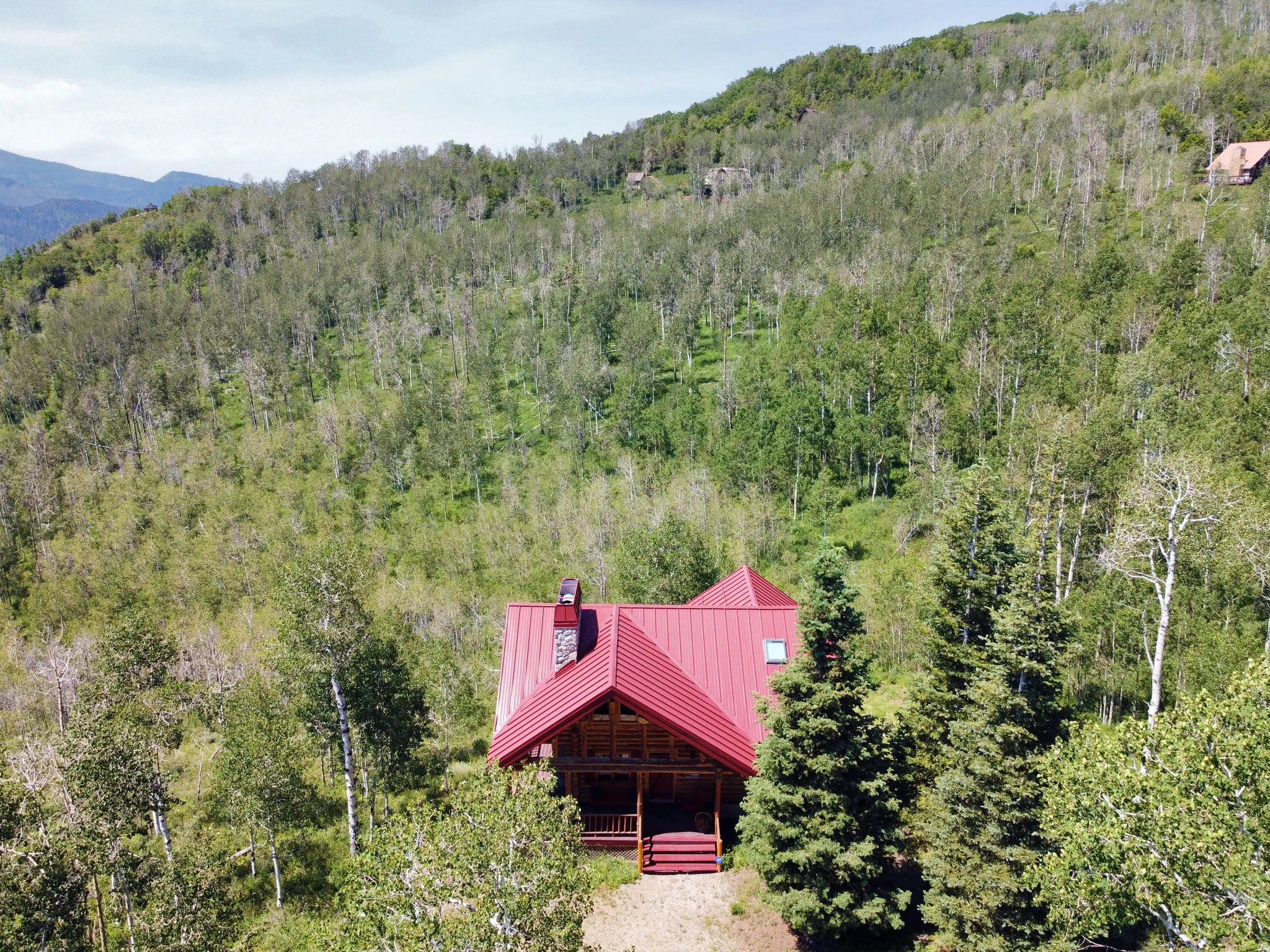 The cabin has a vibrant red metal roof and chimney cap, a stone-clad chimney, and a covered porch.