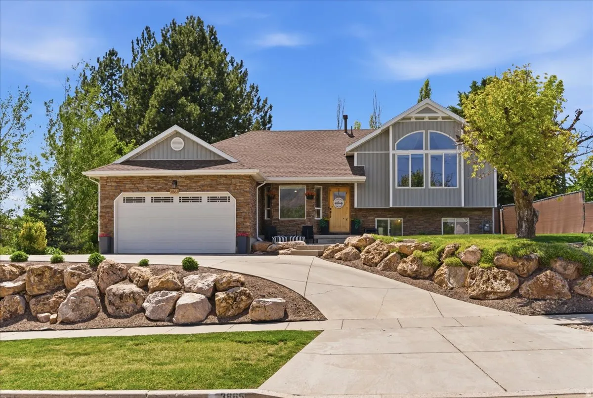 Multi-level residence featuring a two-car garage with exterior lighting, a stone facade