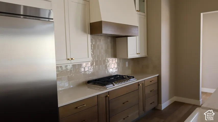 Modern kitchen featuring stainless steel appliances, white cabinetry with bronze hardware accents, quartz countertops, subway tile backsplash, and a gas cooktop with a bronze range hood