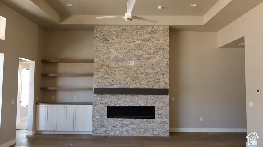 Tray ceiling, stone-clad fireplace with mantel, linear fireplace insert, built-in cabinetry, and floating wood shelves