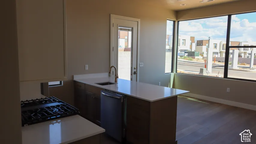 Modern kitchen featuring a gas cooktop, stainless steel sink with contemporary faucet, dark cabinetry with waterfall-edge countertops, and large windows with expansive city views