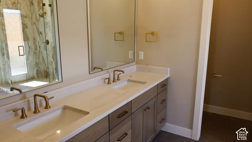Dual-vanity bathroom featuring an expansive quartz countertop, undermount sinks with bronze fixtures, dark cabinetry with ample storage, large framed mirrors, and recessed lighting