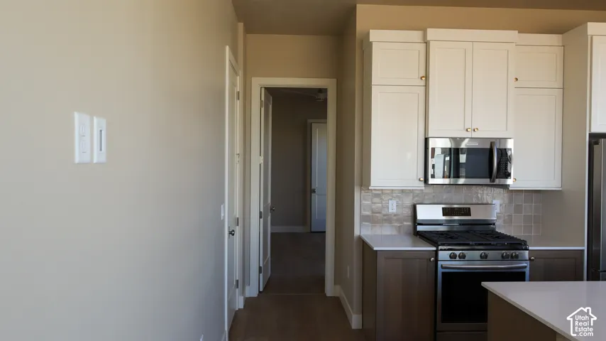 Kitchen featuring stainless steel range with overhead microwave, two-tone cabinetry, tiled backsplash, and light-colored countertops