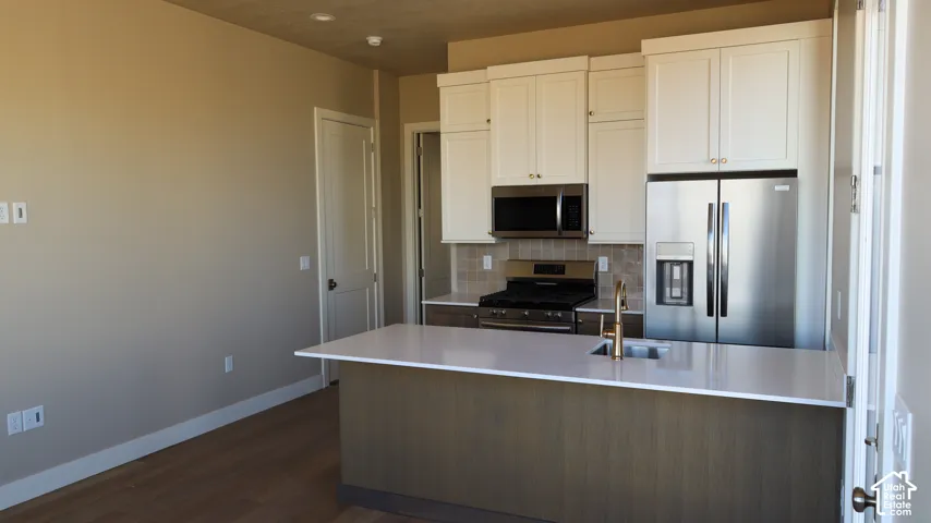 Modern kitchen featuring white cabinetry, stainless steel appliances including a French-door refrigerator and built-in microwave, quartz waterfall island countertop with undermount sink, and dark wood-finish flooring throughout the open living area