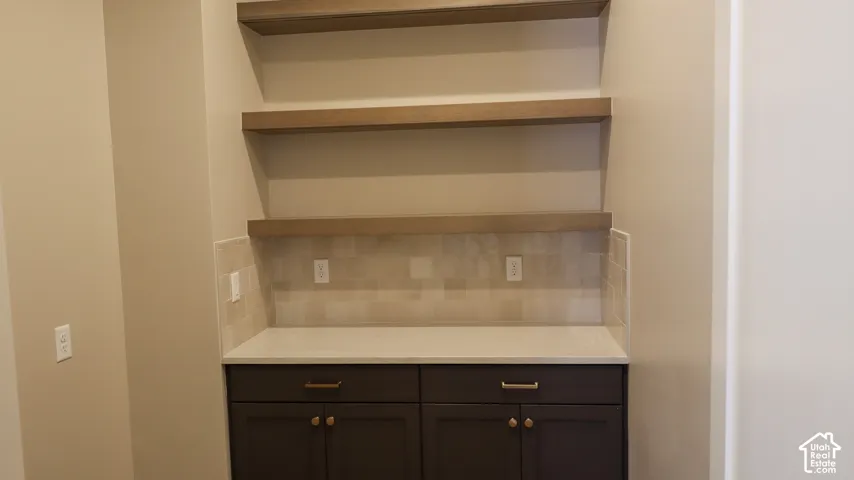 Built-in cabinetry with modern hardware, stone countertop, tiled backsplash, and wood-finish floating shelves