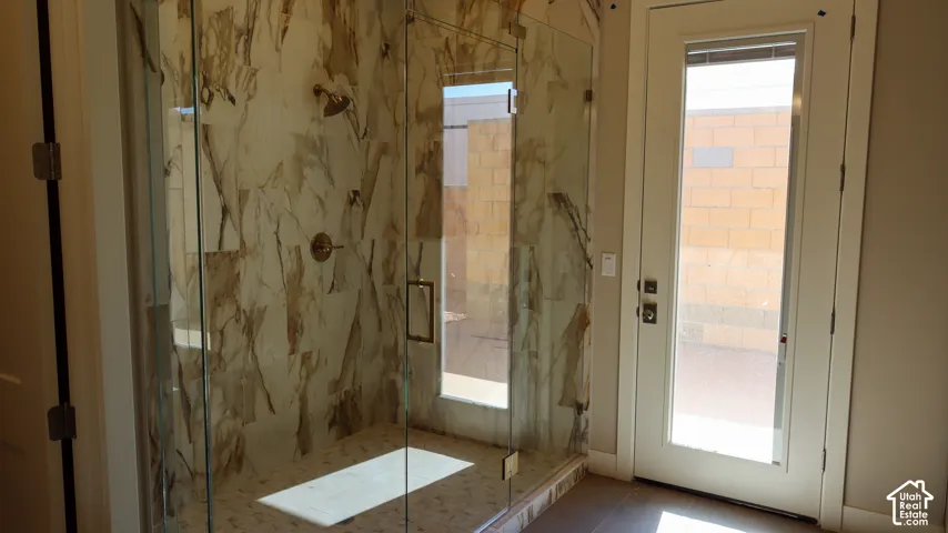 Spa-inspired primary bathroom featuring a frameless glass shower enclosure with marble-look tile surround, a floating vanity with quartz countertop, and dual glass doors opening to outdoor space