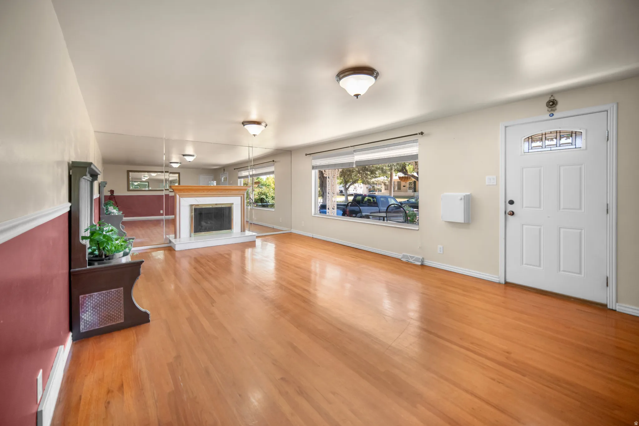 Living area featuring wood-finish flooring, a fireplace with a wood mantle and stone surround, multiple windows, a paneled entry door with an arched glass insert, and semi-flush mount lighting fixtures
