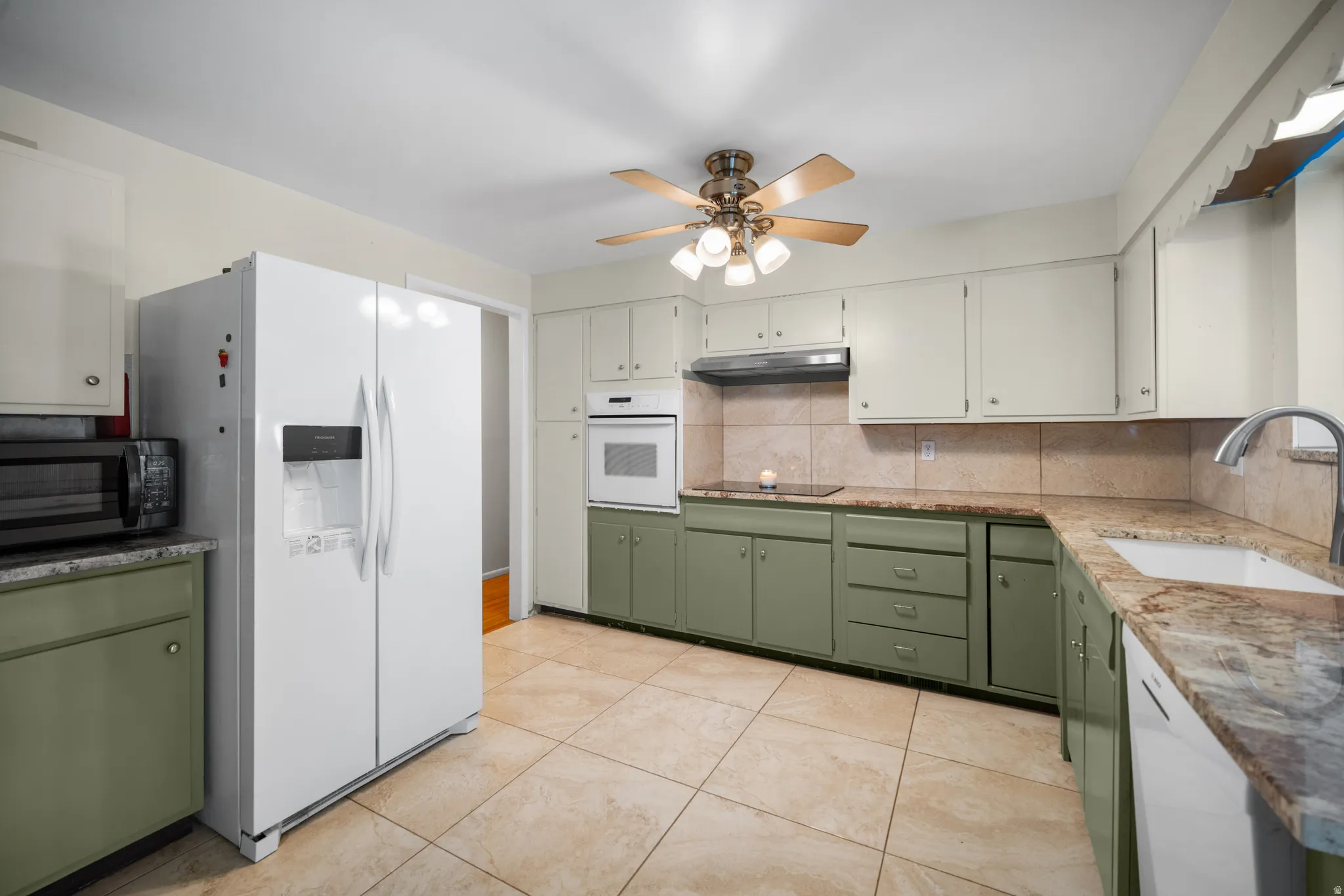Spacious kitchen featuring two-tone cabinetry, stone-finish countertops, tile backsplash, and a built-in oven