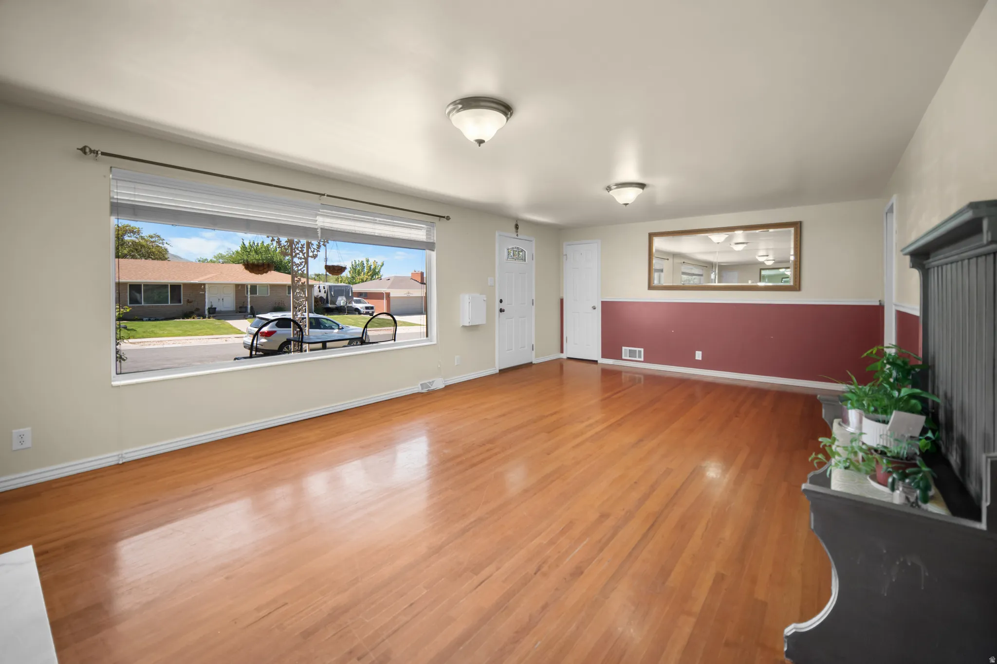 Spacious room featuring wood-finish flooring, a large picture window with blinds, and neutral painted walls with a red wainscoting accent