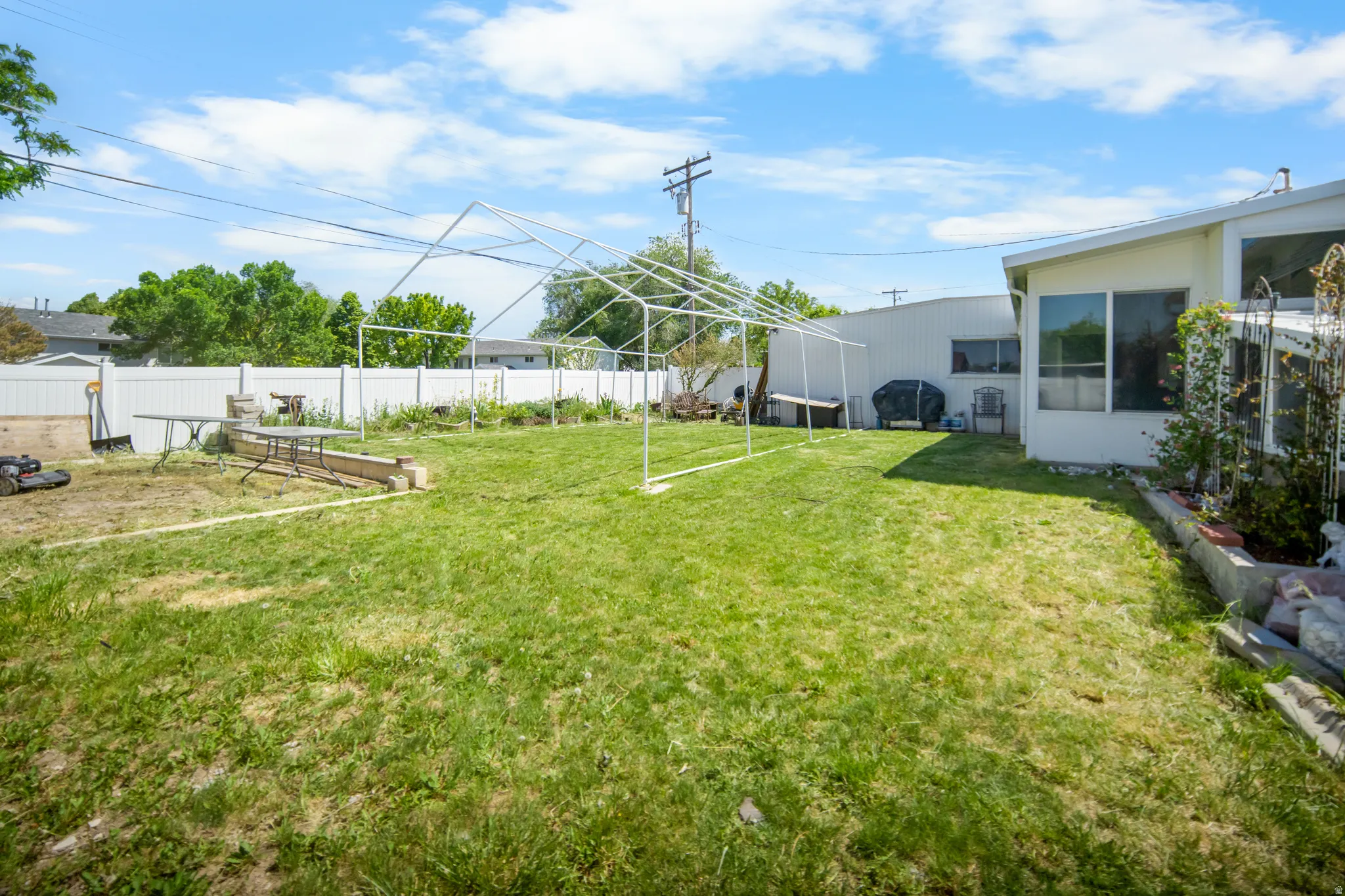 Expansive rear yard featuring green lawn, white privacy fencing, and concrete-block planter boxes